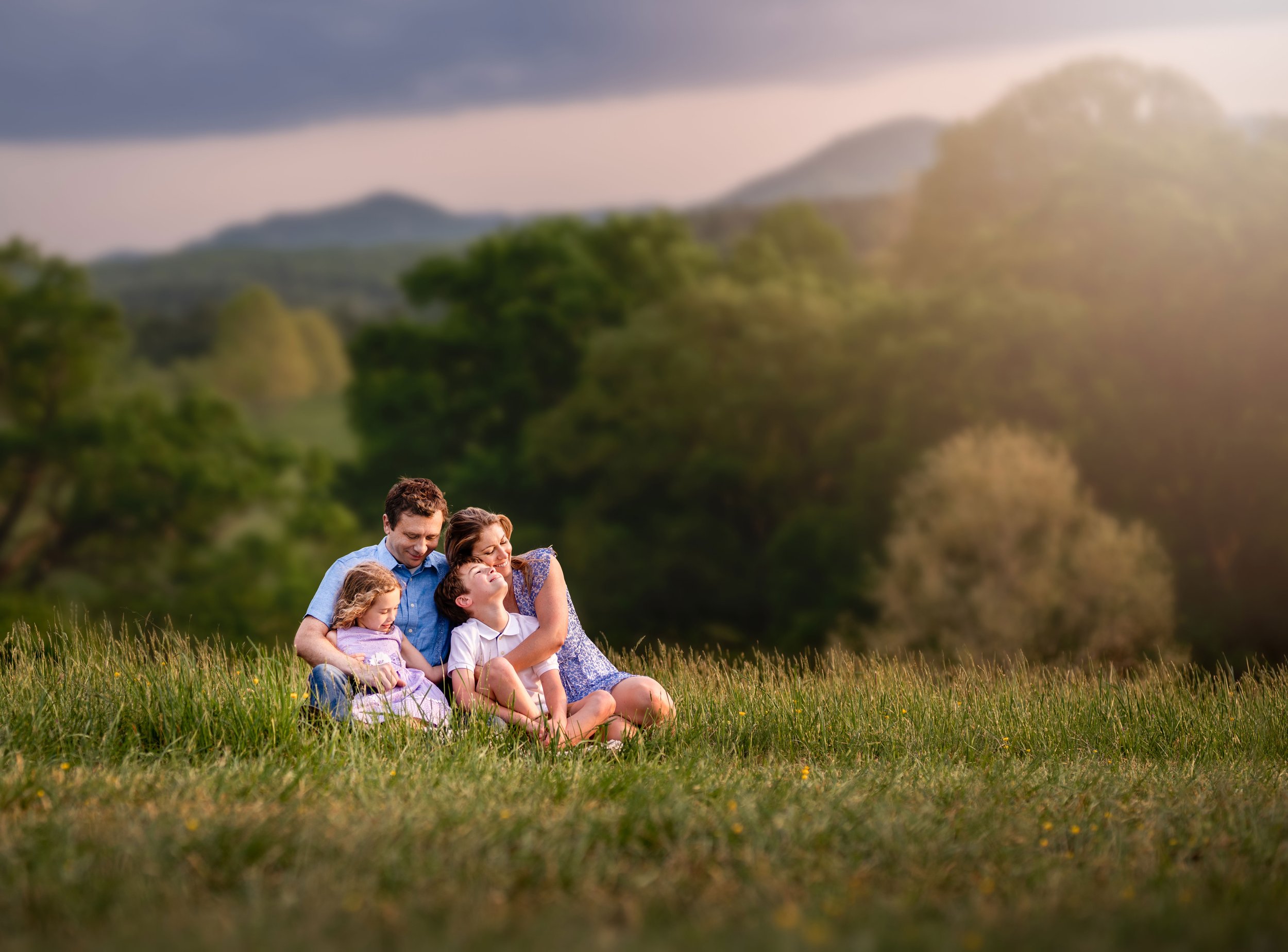 Family snuggling in the grass with mountains in the distance