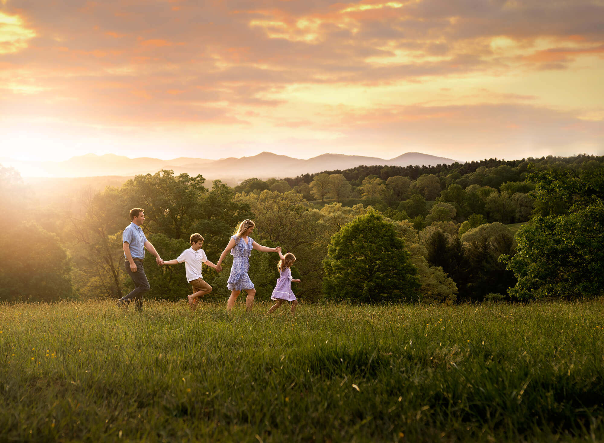 A family walking through a field in front of the mountains at sunset.