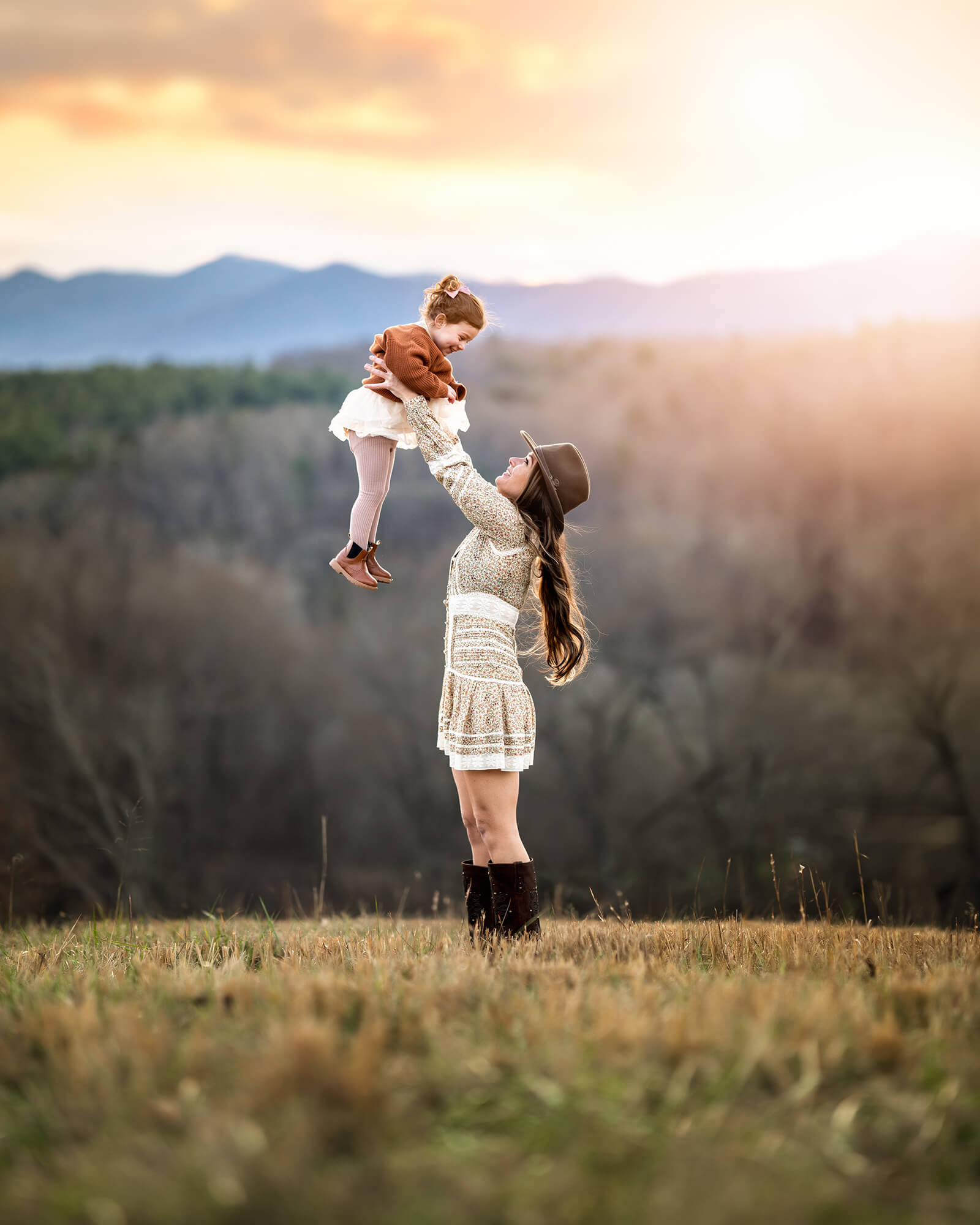 A mom twirling her daughter in a grassy field in front of the mountains