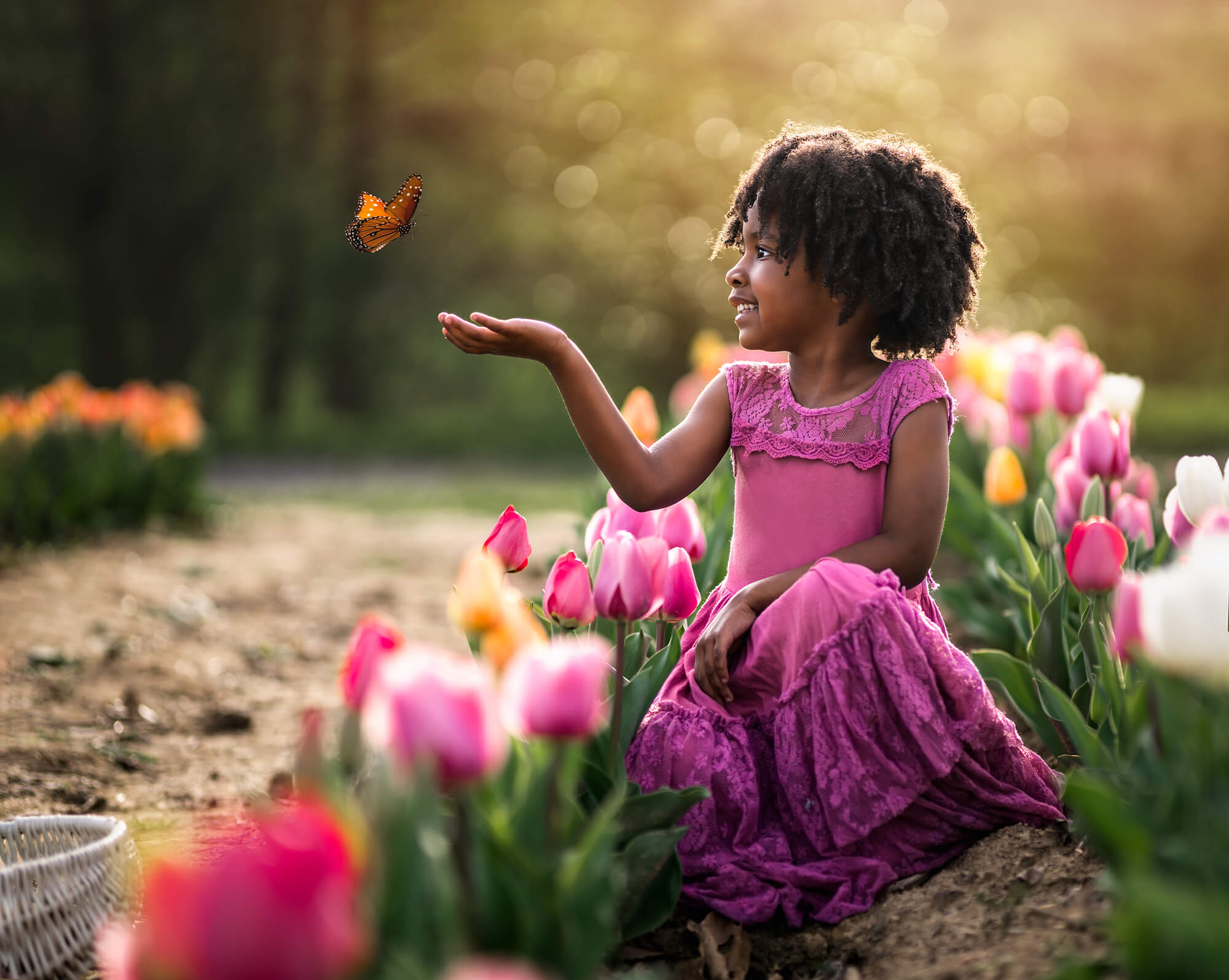 a little girl in a pink dress catching a butterfly surrounded by tulips.