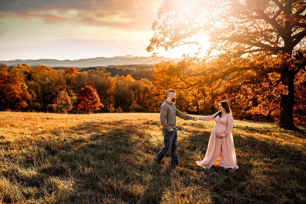 An expecting couple dancing in the sunlight with mountains in the distance for an Asheville Maternity Photography session