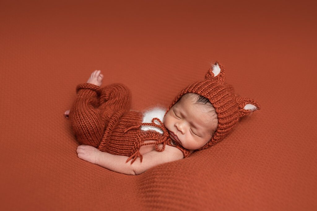 Newborn baby dressed as an orange fox and sleeping on an orange blanket