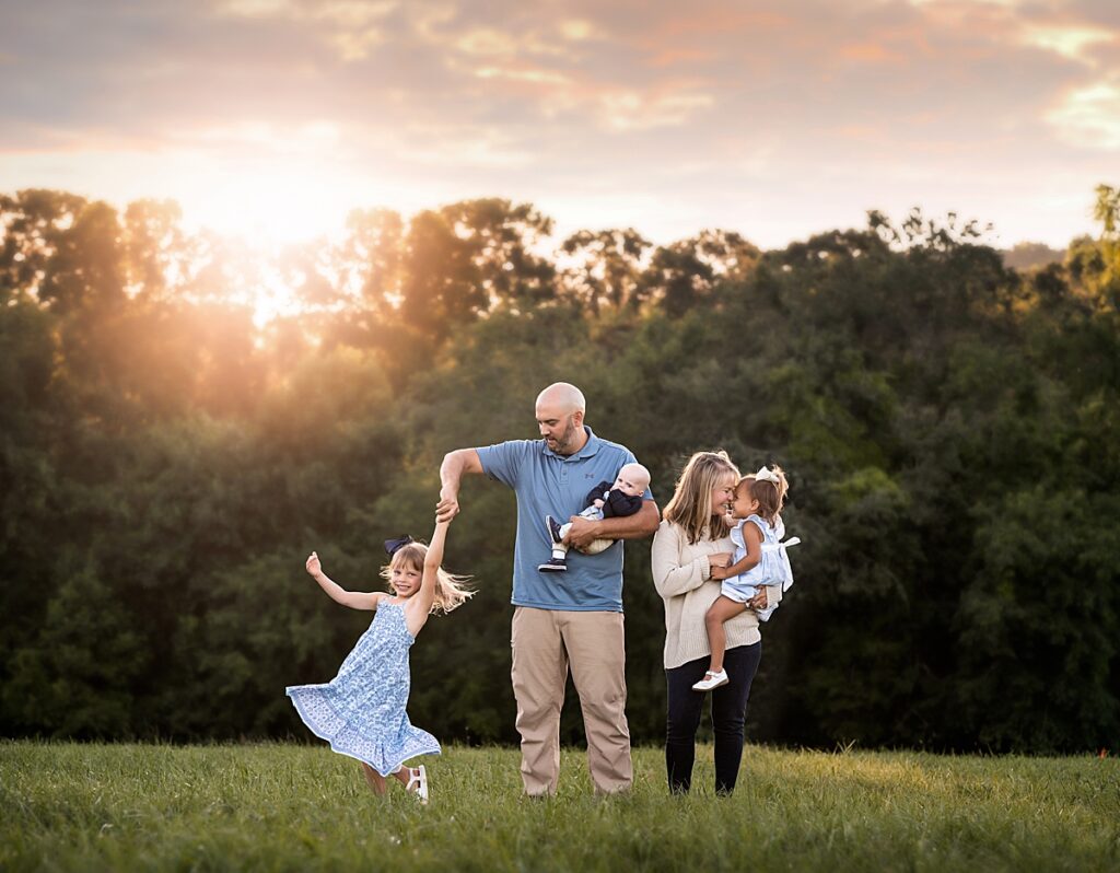 An adorable family of five laughing, twirling and playin in a meadow at sunset near Asheville