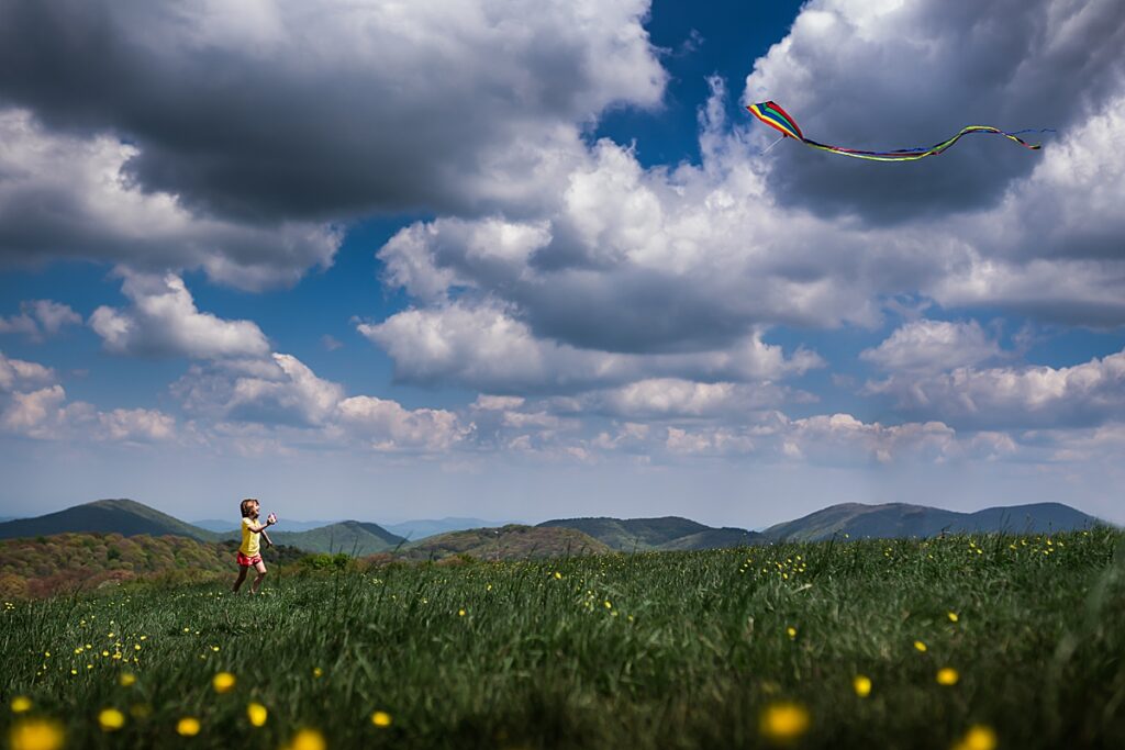 A young girl running through the grass and flying a kite on top of Max patch near Asheville NC