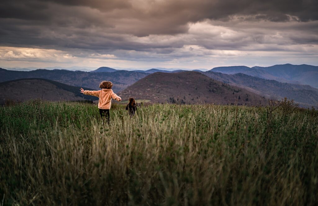 Two young girls running through the tall grass while hiking on a kid Friendly hike in Asheville NC