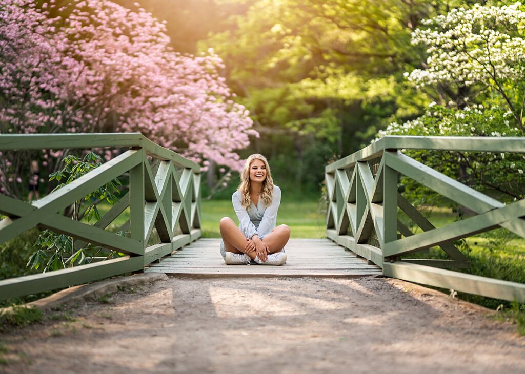 A gorgeous girl sits on a bridge with pink flowers blooming behind her during her senior session with Asheville Senior PHotography