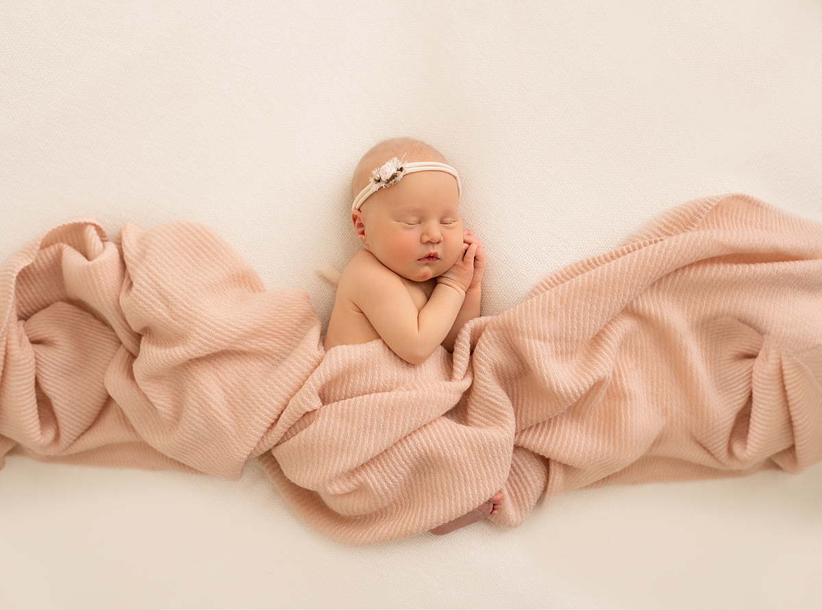 A newborn baby girl swaddled in a pink blanket and sleeping peacefully