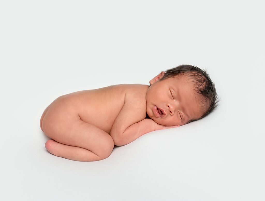 a newborn baby in his birthday suit laying on his tummy and sleeping on a white blanket