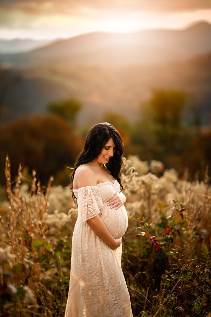 A stunning expecting mama to be in a cream dress cradles her baby bump. 