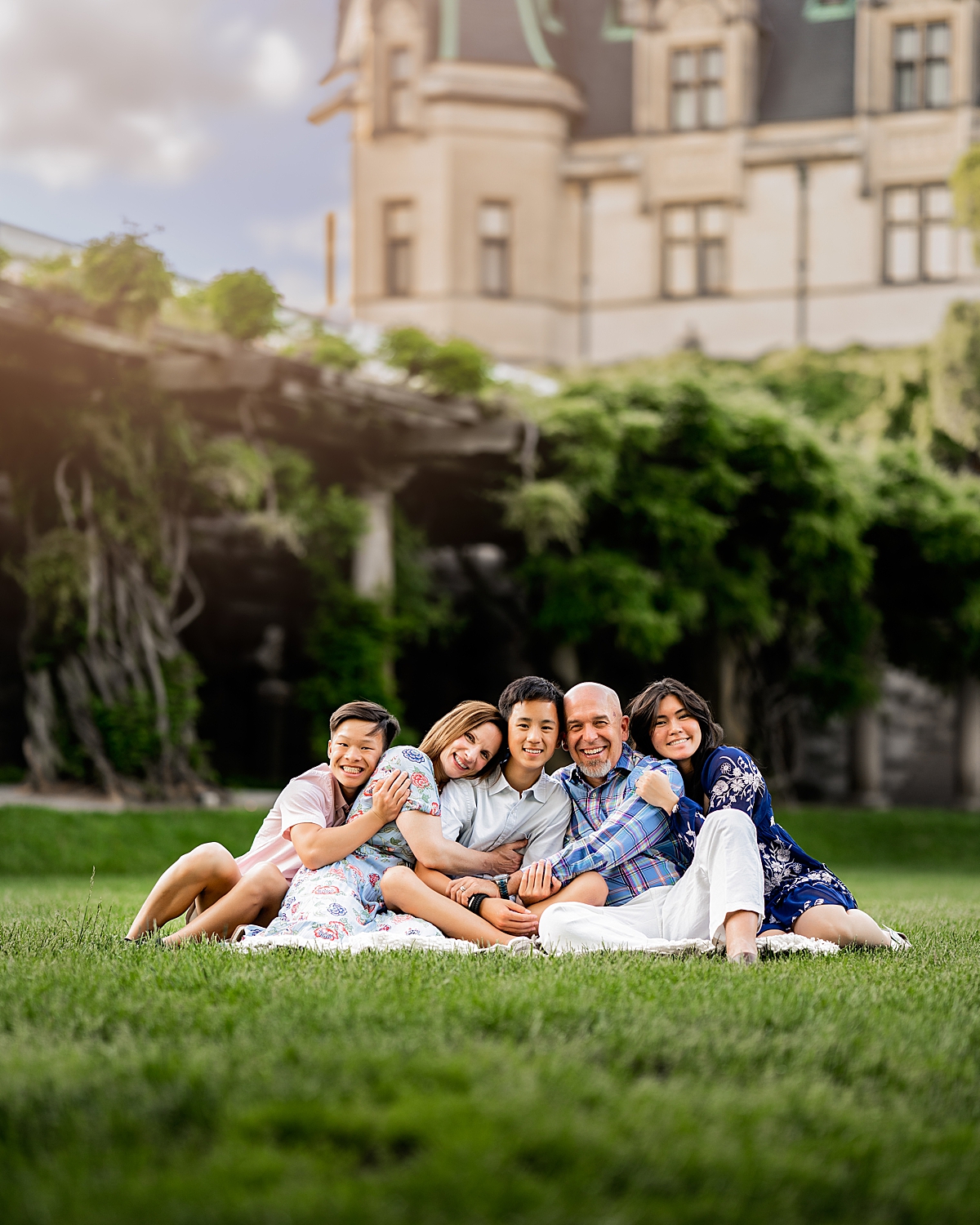 A family of five cuddles and smiles on a blanket in front of the biltmore house in Asheville NC