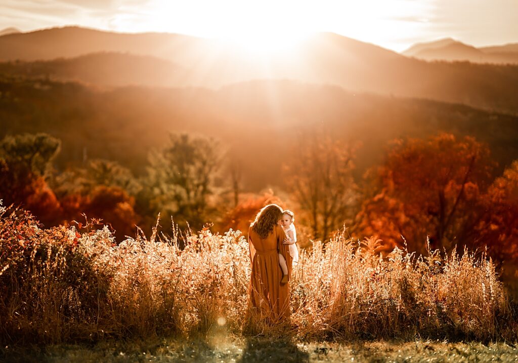 A mom snuggles her daughter in the golden light of sunset with mountains in the distance near Asheville 