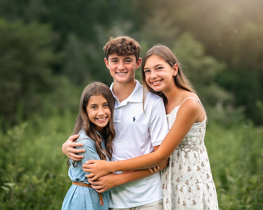 Three siblings snuggle and smile for the camera during a portrait session with the Best Asheville Family Photographer