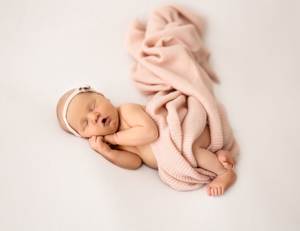 A newborn baby girl wrapped in a pink blanket with a pink headband and sleeping