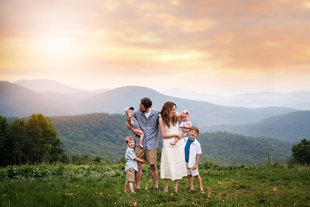 A family of 6 snuggles and laughs while standing on a mountain top near Asheville