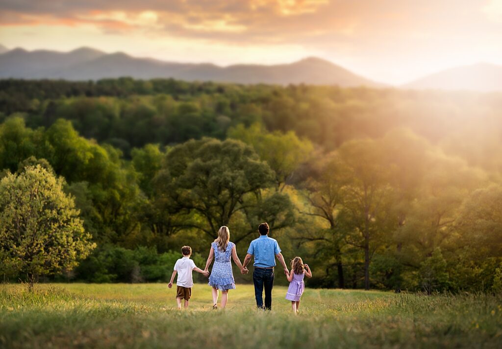 A family of four walking in a meadow with mountains in the distance during a session with a family photographer in Asheville