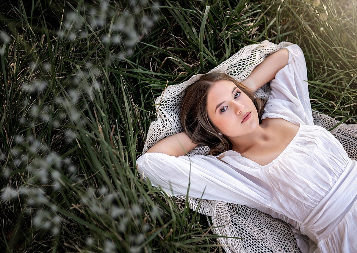 a beautiful young girl in a white dress laying in the grass with white flowers around her