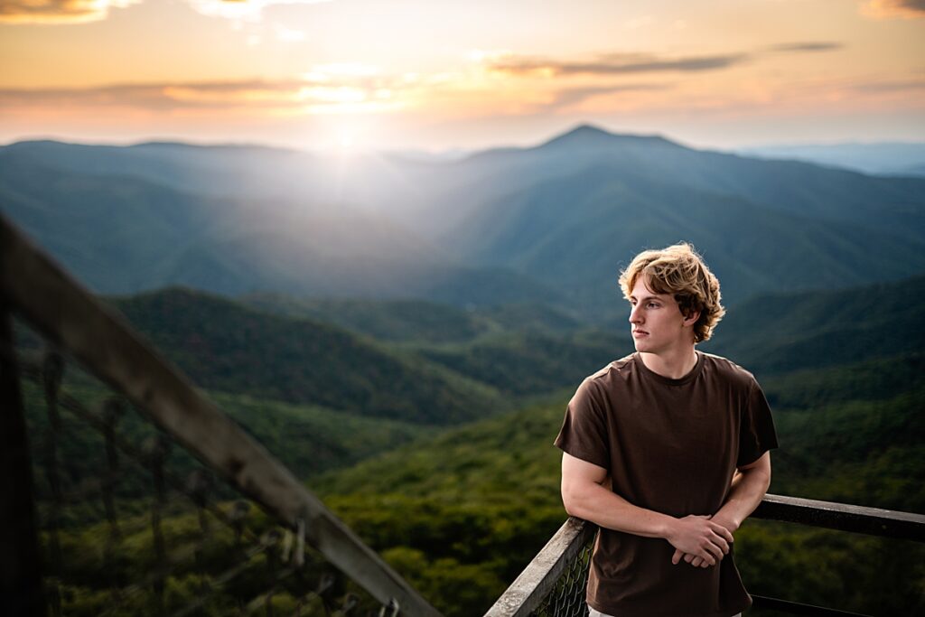 A young man stands on top of frying pan tower in the mountains near Asheville North Carolina as the sun sets behind him