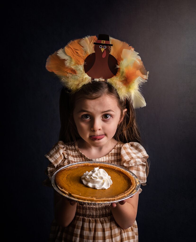 a little girl with a thanksgiving headband holds a pumpkin pie