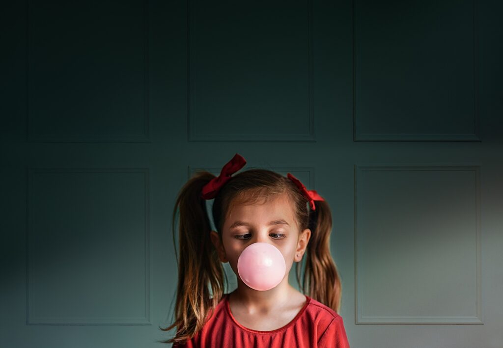 a little girl in a red dress with pig tails blows a large bubble with pink bubble gum - kid friendly restaurants in Asheville 
