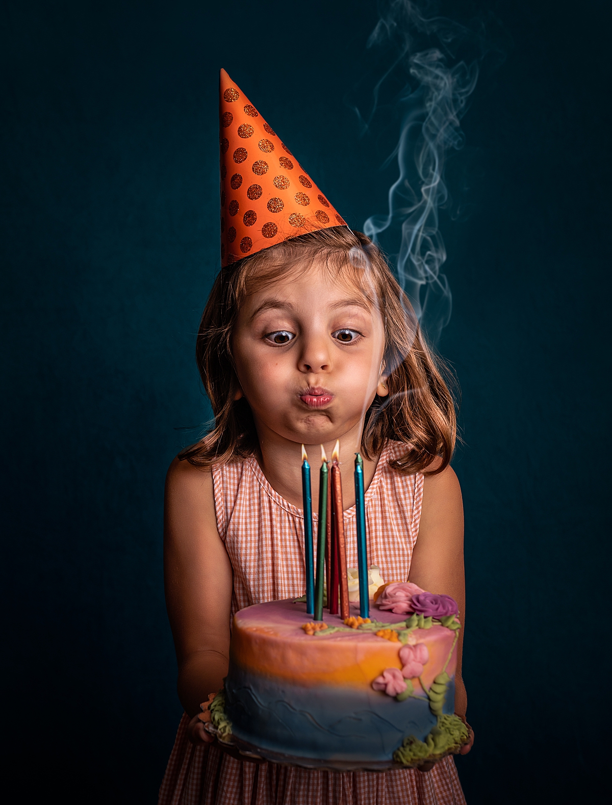 a little girl with an orange birthday hat on blowing out the candles on her birthday cake.