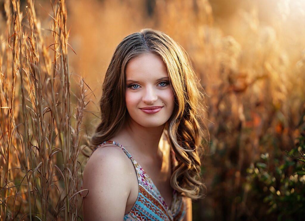 Beautiful senior girl sitting in the tall golden grass 