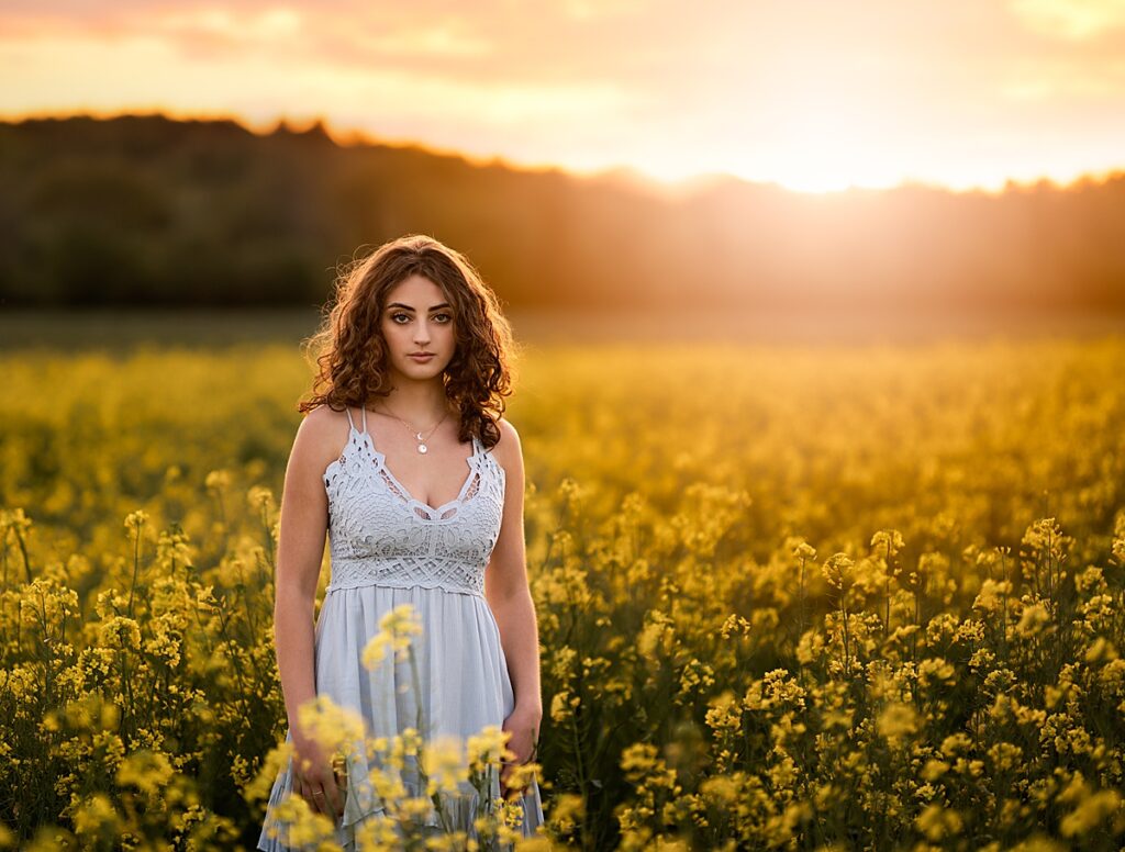 A stunning young girl in a blue dress standing in a field of yellow flowers during her senior photo session in Asheville 