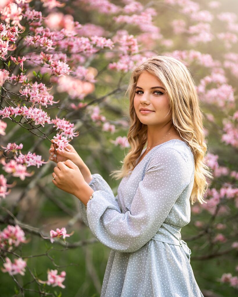 a pretty young girl standing in front of a tree with beautiful pink flowers 