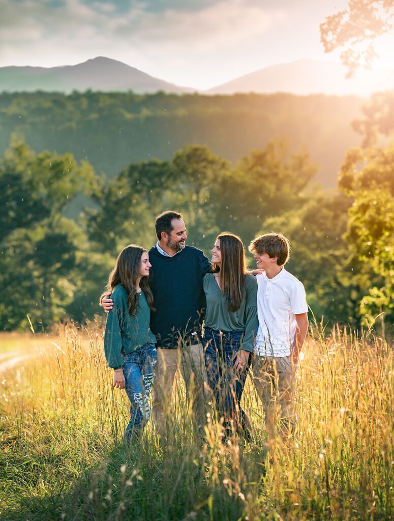 A family standing in the golden grass at sunset with mountains behind them near Asheville NC
