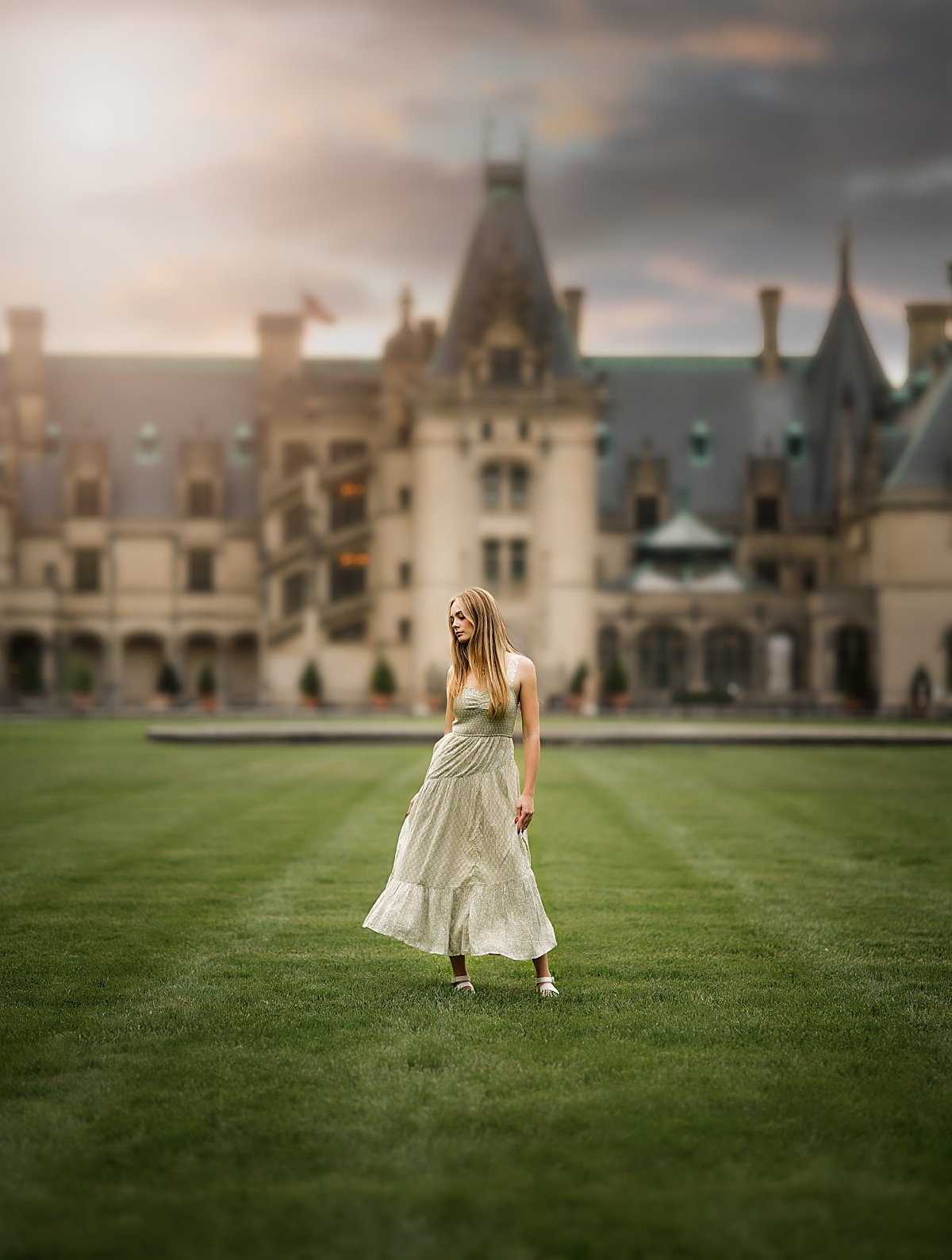 A young girl in a long green dress stands in front of the Biltmore Estate