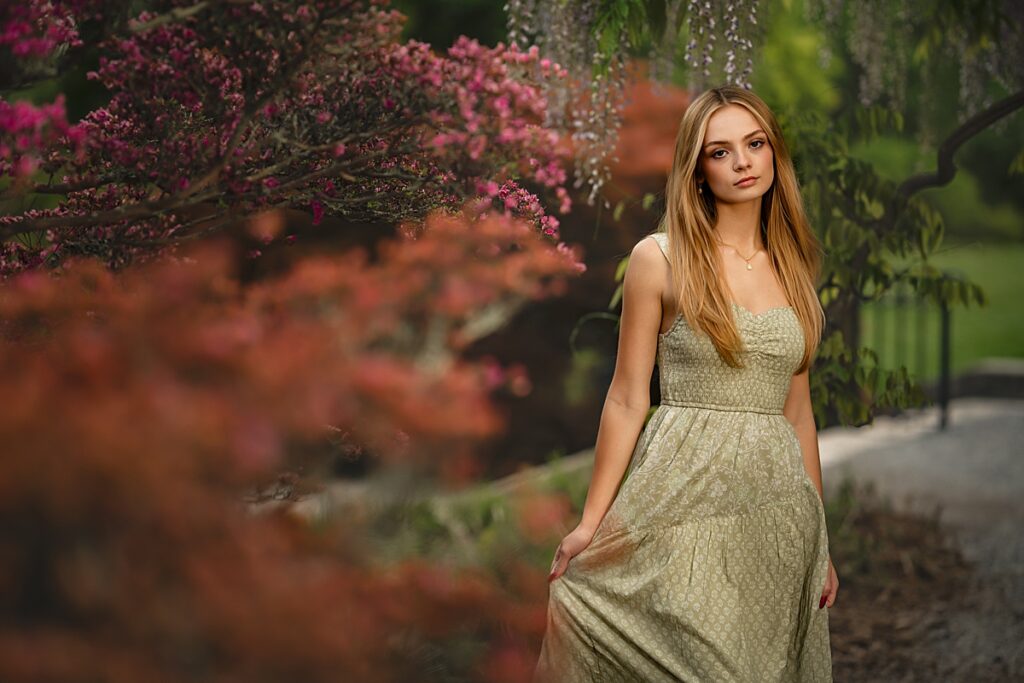 A young girl in a green dress stands in the garden at the Biltmore Estate and smiles during her senior photo session