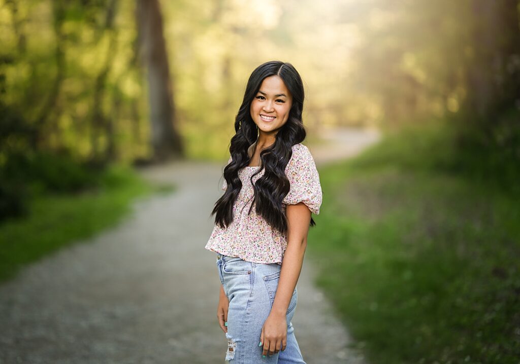 A young girl in jeans and a flowy tee walks down a path with the sun behind her during her Asheville Senior Photo Session 