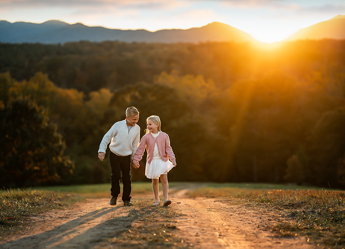 A brother and sister run through a field as the sun sets behind them on the Biltmore Estate