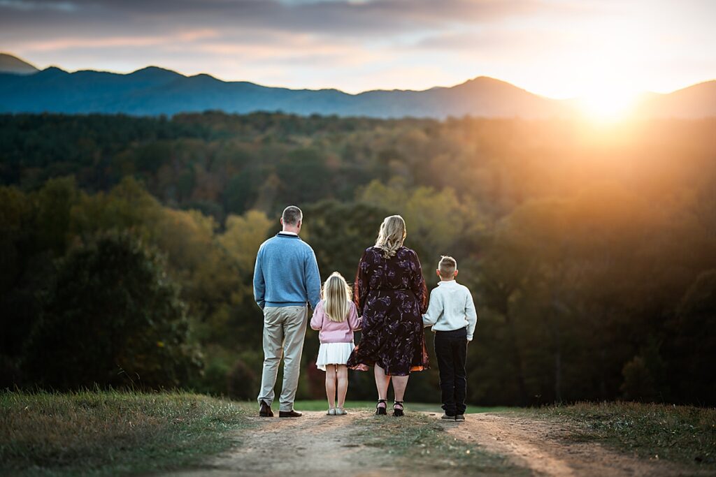 A mom, dad and two siblings walk along a path toward the mountains at sunset