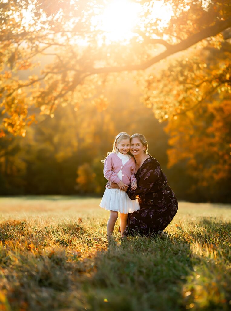 a mother and daughter stand beneath and tree and cuddle as the golden sun sets behind them