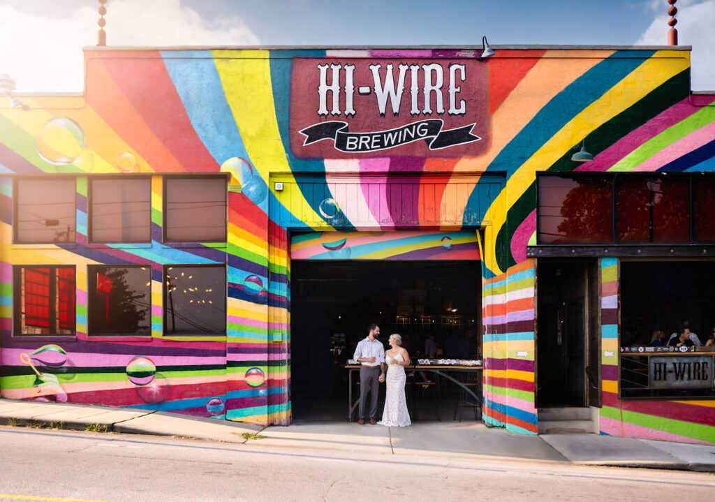 a bride and groom cheers with a beer while standing in the door way of hi wire brewing in Asheville NC 